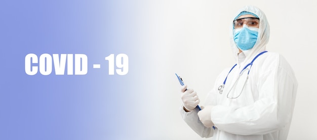 covid-19 text and portret of doctor in protective medical suit, biological hazard, face mask doctor with stethoscope writes on tablet. medical healthcare concept coronavirus, covid, pandemic.