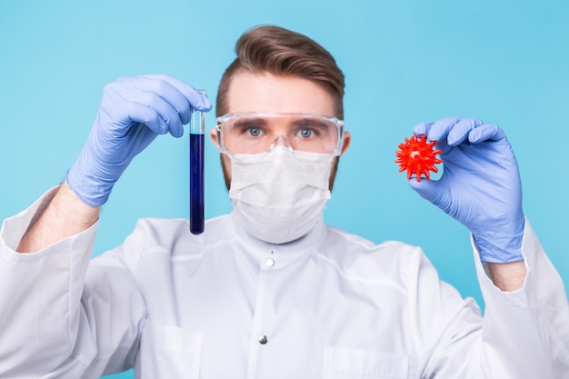 Covid-19, Vaccine development, pandemic, outbreak and medicine concept - Man scientist in flu mask and protective gloves holding a model of coronavirus and test tube.