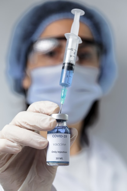 COVID-19 vaccine in researcher hands, unrecognizable female doctor holds syringe and bottle with vaccine for coronavirus cure. 