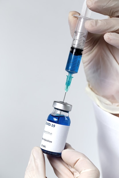 Вакцина COVID-19 в руках исследователя, до неузнаваемости женщина-врач держит шприц и бутылку с вакциной для лечения коронавируса.