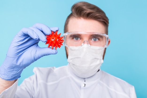 Covid-19, vaccinontwikkeling en medicijnconcept - Man wetenschapper in griepmasker en beschermende handschoenen met een model van coronavirus.