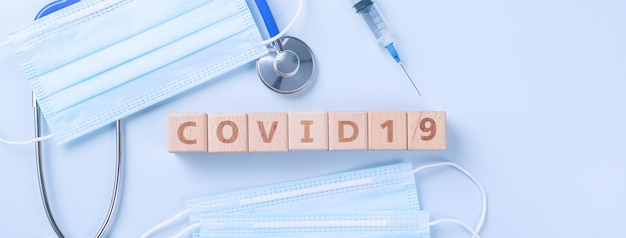 COVID-19ワードの木製キューブ、マスク、医療機器、世界的大流行の感染と予防の概念、上面図、フラットレイ、オーバーヘッドデザイン