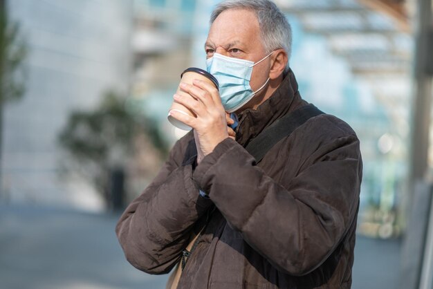 Covid coronavirus concept gemaskerde oudere man die buiten koffie drinkt