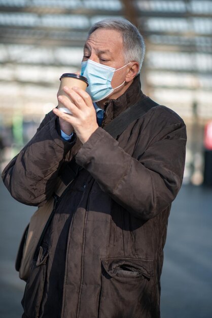 Covid coronavirus concept gemaskerde oudere man die buiten koffie drinkt