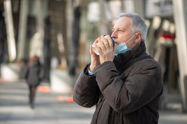 Covid coronavirus concept gemaskerde oudere man die buiten koffie drinkt