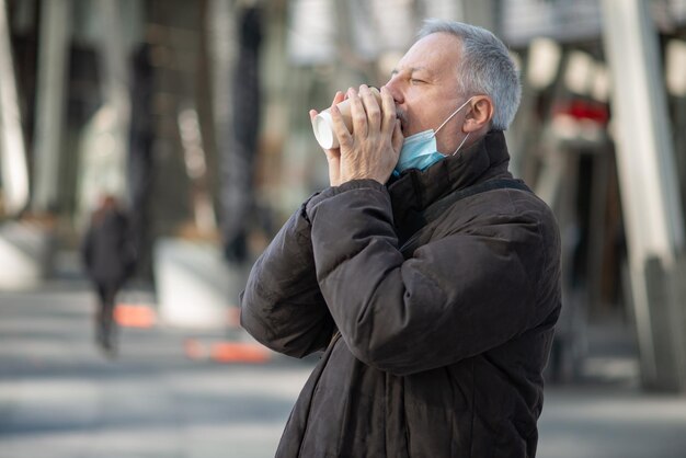 Covid coronavirus concept gemaskerde oudere man die buiten koffie drinkt