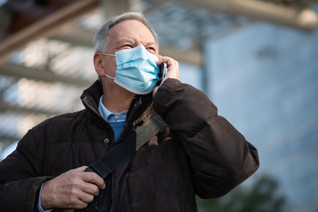 Covid coronavirus concept gemaskerde oudere man die buiten op zijn smartphone praat