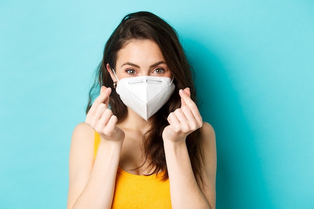 Covid coronavirus and social distancing cute young woman wearing health face mask and showing finger hearts