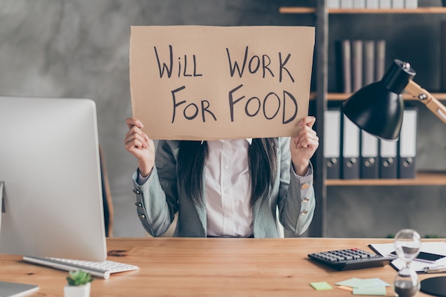 Foto concetto di crisi della povertà dell'economia covid. la ragazza frustrata disperata ha bisogno di un lavoro tenere il testo in cartone funzionerà per il cibo indossare giacca blazer sedersi tavolo scrivania nella postazione di lavoro sul posto di lavoro