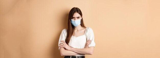 Covid en lifestyle-concept boze vrouw kijkt met verachting en draagt een medisch masker met gekruiste armen op de borst