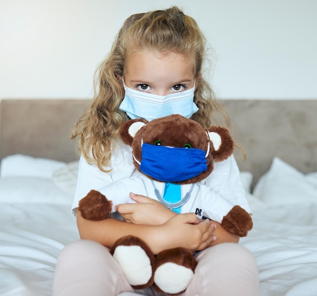 Covid girl and teddy bear love and care for safety and awareness in pandemic quarantine at home Portrait of a little kid playing doctor holding cute fluffy toy with mask for healthcare in pandemic