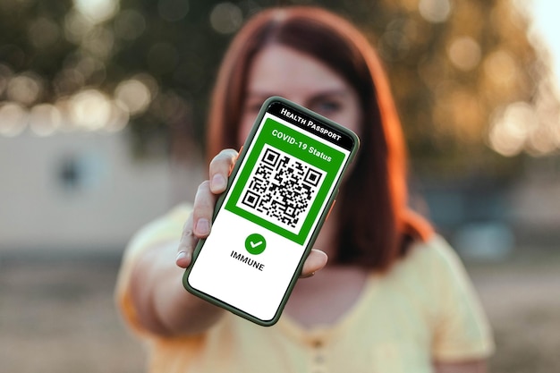 旅行期間中のデジタルヘルスパスポートアプリを備えたCovidパンデミックコロナウイルストラベラーガールスマートフォン...