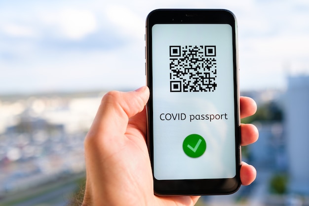 Covid pass with qr code on the screen in smartphone in mans hand on the background of cityscape