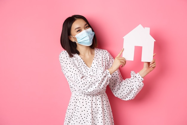 Covid real estate and lifestyle concept cute asian woman in face mask selling houses showing model o...