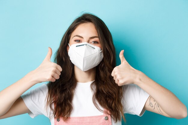 Covid social distancing and lockdown concept close up of young woman in respirator showing thumbs up...