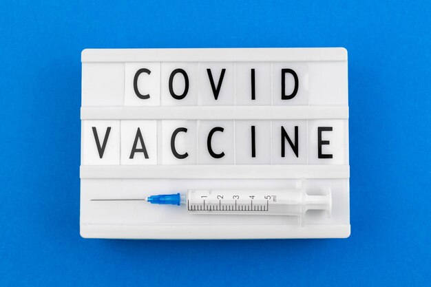 Covid vaccin coronavirus sms, inscriptie close-up, lightbox met belettering en medische spuit, bovenaanzicht en platliggende foto