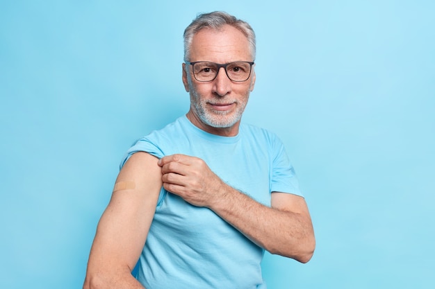 Covid vaccination concept. serious bearded grey haired man shows place of inoculation adhesive plaster on arm