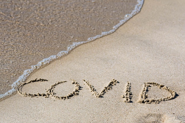 사진 코로나 바이러스 발병 중에 그것을 지우거나 취소하는 파도와 함께 해변의 모래에 covid가 쓰여져 있습니다.