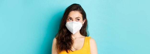 Covid19 coronavirus and social distancing Close up portrait of young modern woman in respirator looking at upper left corner logo standing against blue background
