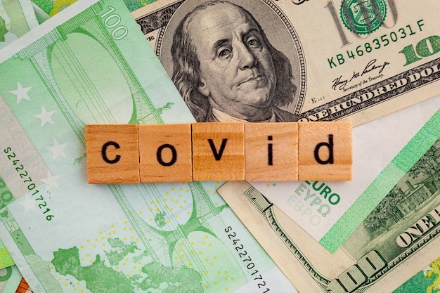COVID19 inscription on wooden cubes on the texture of us dollars and euro banknotes