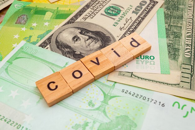 COVID19 inscription on wooden cubes on the texture of us dollars and euro banknotes