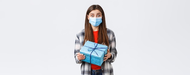 Covid19 stile di vita vacanze e concetto di celebrazione eccitata ragazza di compleanno carina che tiene una scatola avvolta curiosa cosa dentro riceve un regalo indossando una maschera medica per prevenire l'epidemia di coronavirus
