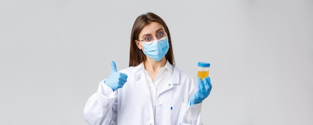 Covid19 medical research diagnosis healthcare workers and\
quarantine concept doctor or clinic lab employee holding patient\
urine sample wear medical mask and gloves thumbup