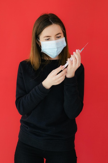 COVID19 Pandemic Coronavirus Young girl on red background face mask protective holding a syringe C