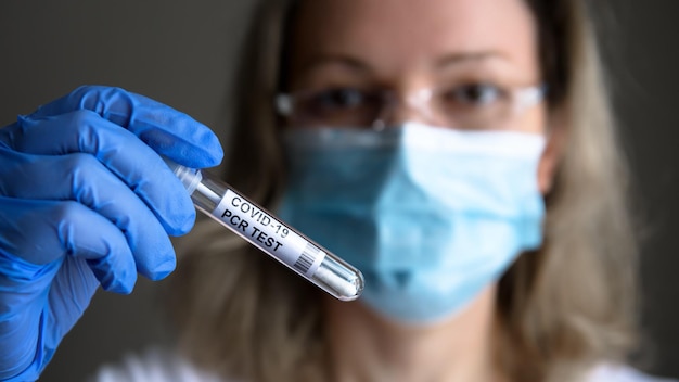 COVID19 PCR test tube in doctor hand woman in medical mask holds coronavirus swab collection kit