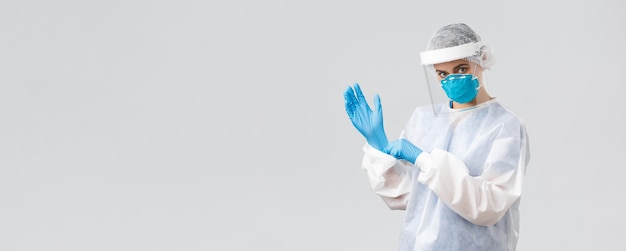 Covid19 preventing virus health healthcare workers and quarantine concept Determined young woman doctor nurse in PPE protective equipment face mask put on rubber gloves working on vaccine