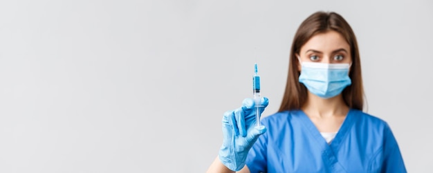 Covid19 preventing virus health healthcare workers and quarantine concept Seriouslooking confident female doctor or nurse in blue scrubs medical mask showing syringe with coronavirus vaccine