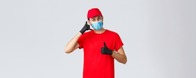 Covid19 selfquarantine online shopping and shipping concept Friendly delivery guy in gloves and face mask carrier uniform show phone asking call company order delivery thumbup