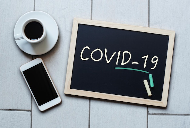 칠판에 쓰여진 COVID19 텍스트 COVID19 우한 신종 코로나바이러스 폐렴 분필 보드, 커피와 휴대전화