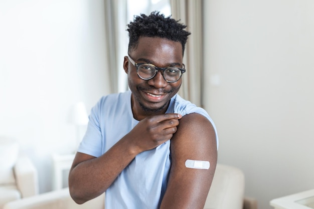 Photo covid19 vaccination portrait of happy vaccinated african man showing his arm after coronavirus antiviral vaccine shot covid immunization campaign concept