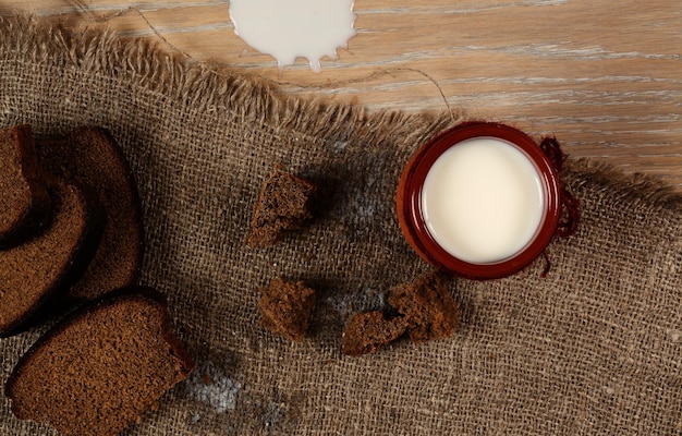 Cow milk in a rustic clay glass with rye bread on a sackcloth