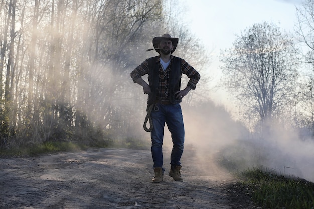 A cowboy in a hat and vest is standing in a thick smoke on the road