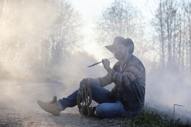 A cowboy in a hat and vest is standing in a thick smoke on the road