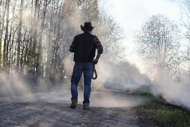 A cowboy in a hat and vest is standing in a thick smoke on the road