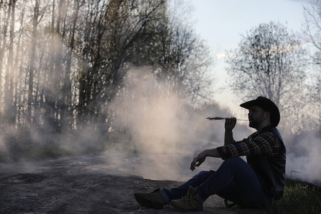 A cowboy in a hat and vest is standing in a thick smoke on the road