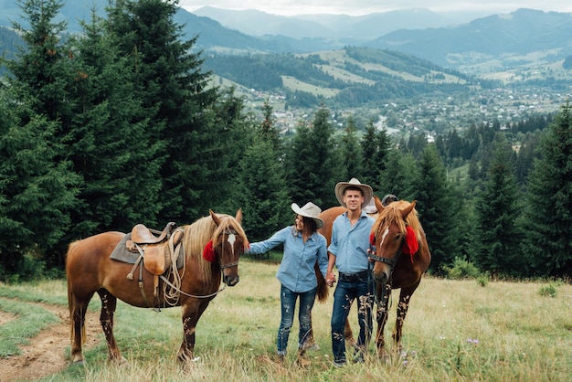 Un cowboy e la sua ragazza camminano lungo un sentiero con i loro cavalli in montagna