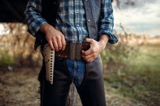 Cowboy in jeans and leather clothes with his hand on the revolver