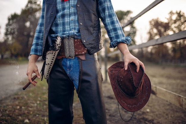 Cowboy in leather clothes poses with cigare in the horse corral