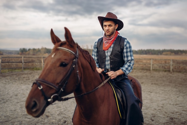 Cowboy in leather clothes riding a horse on farm