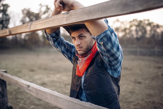 Foto cowboy in giacca di pelle e cappello pone sul ranch