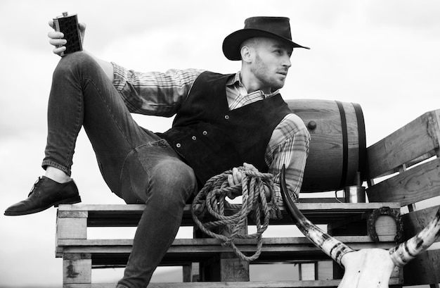 Foto cowboy op de ranch knappe man in cowboy hoed en retro vintage outfit man die whiskey drinkt
