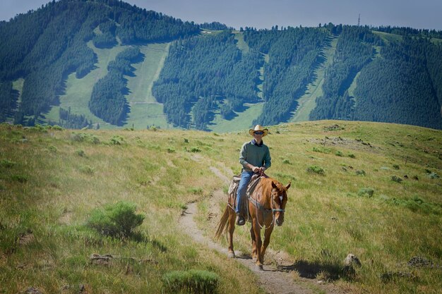 Foto cowboy a cavallo sul campo contro la montagna