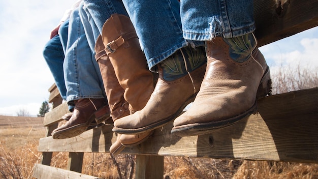 Cowboys and cowgirls sitting on wooden fence.