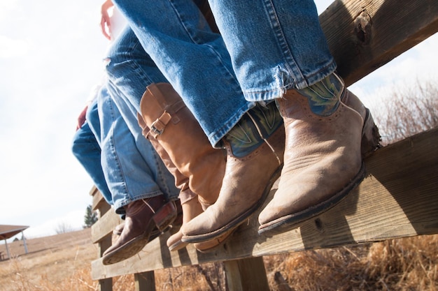 Cowboys en veedrijfsters die op houten omheining zitten.