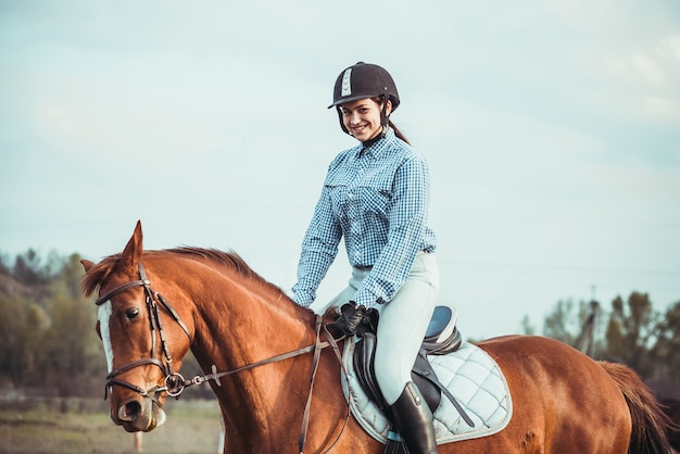 Cowgirl in a hat standing near a horse in a field