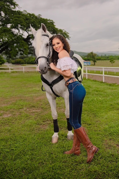 cowgirl next to her beautiful white horse in the field